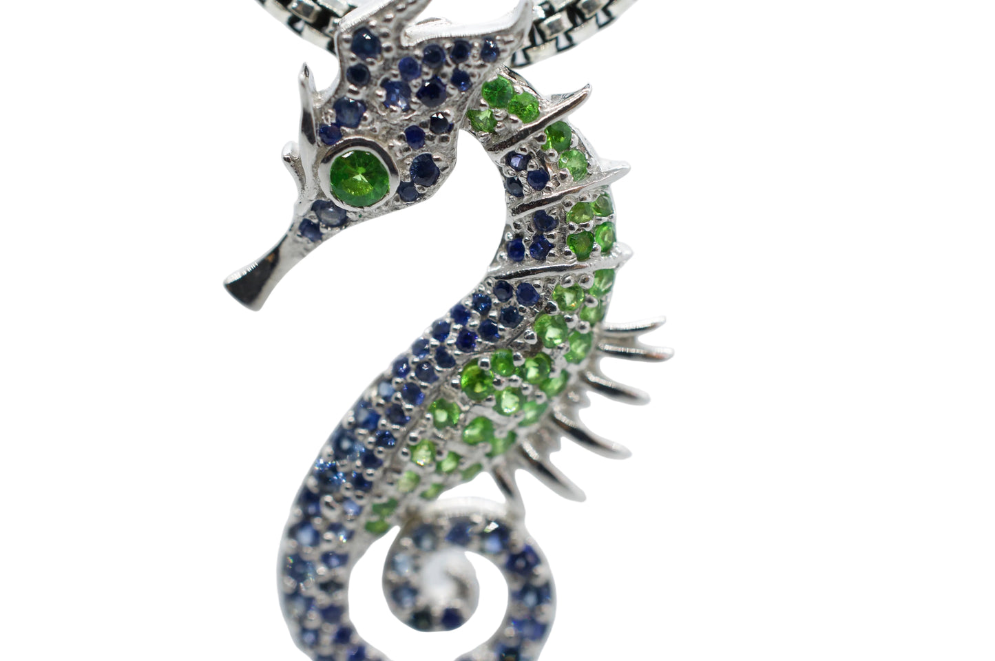 Seahorse-shaped jewelry with green and blue gemstones on a white background